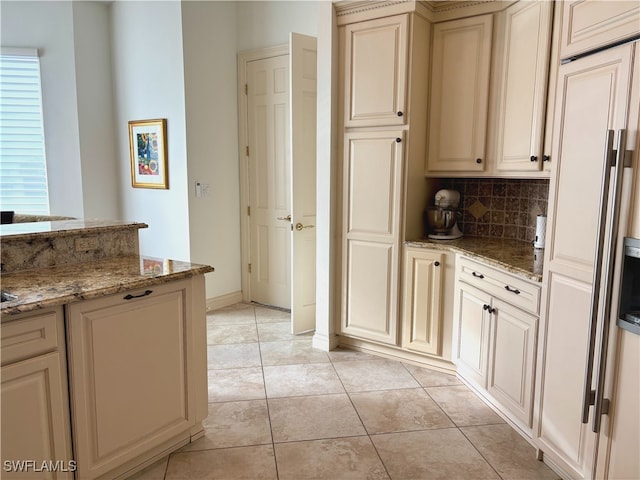 kitchen with light tile patterned floors, tasteful backsplash, baseboards, light stone counters, and cream cabinetry