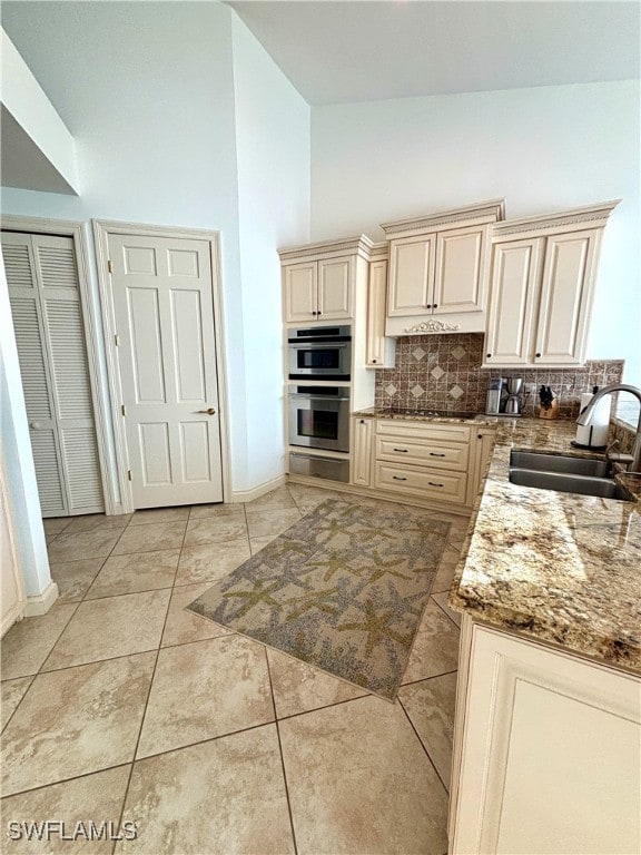 kitchen with tasteful backsplash, cream cabinetry, double oven, high vaulted ceiling, and a sink