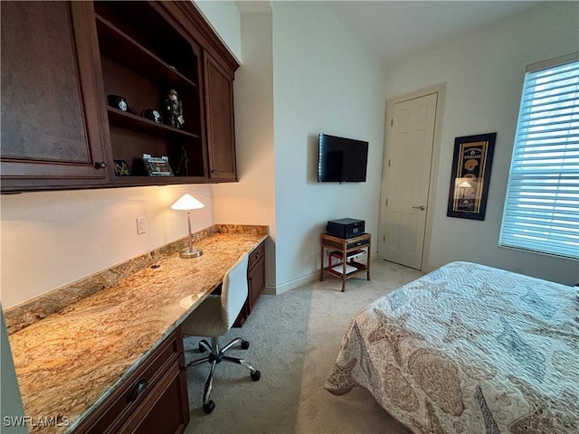 bedroom with built in study area, light carpet, and baseboards