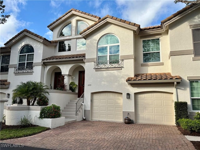 mediterranean / spanish-style house with an attached garage, a tile roof, decorative driveway, and stucco siding