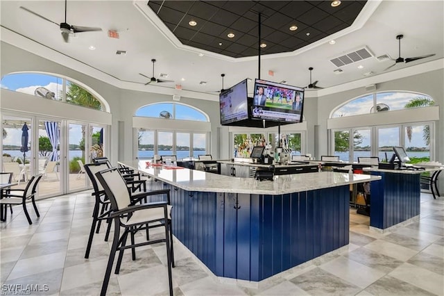 kitchen featuring a high ceiling, a tray ceiling, a spacious island, light stone countertops, and crown molding