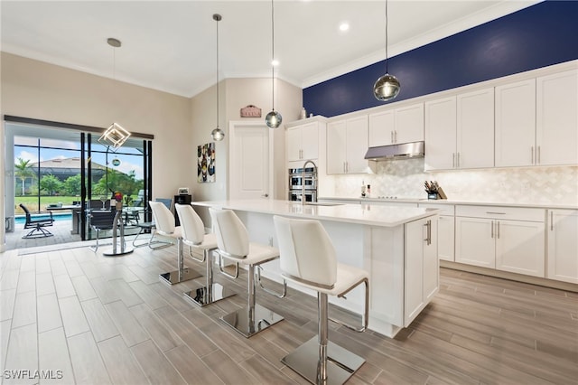 kitchen featuring a kitchen bar, hanging light fixtures, a center island with sink, and white cabinetry