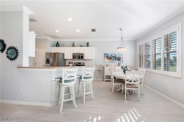 kitchen with appliances with stainless steel finishes, pendant lighting, white cabinetry, a breakfast bar area, and kitchen peninsula