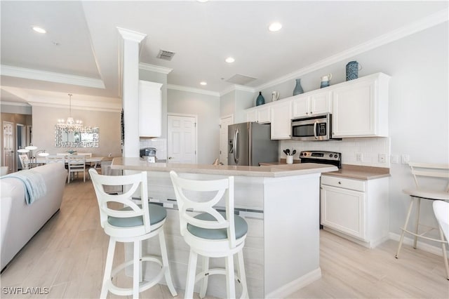 kitchen with decorative light fixtures, light hardwood / wood-style flooring, appliances with stainless steel finishes, a kitchen breakfast bar, and white cabinets