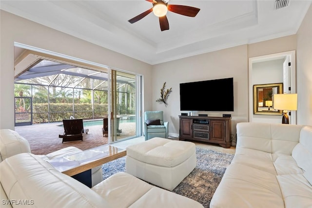 living room with ceiling fan, a tray ceiling, and ornamental molding