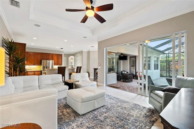 living room with light tile patterned floors, a raised ceiling, crown molding, and a healthy amount of sunlight