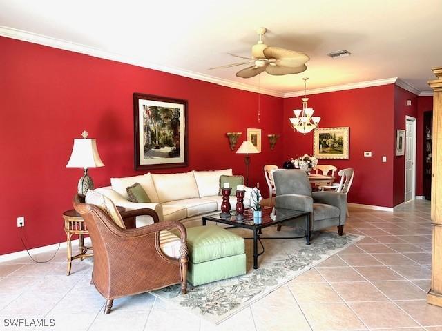 living room with tile patterned flooring, ornamental molding, and ceiling fan with notable chandelier