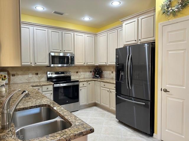 kitchen with appliances with stainless steel finishes, stone countertops, sink, decorative backsplash, and light tile patterned floors