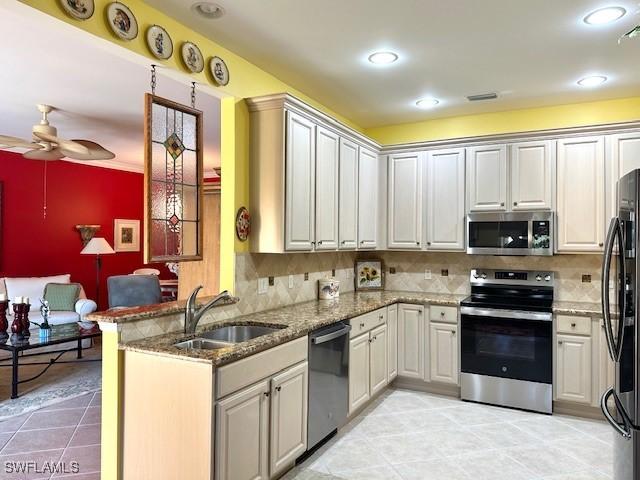 kitchen featuring appliances with stainless steel finishes, kitchen peninsula, sink, ceiling fan, and light stone counters