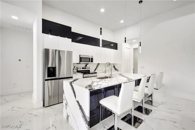 kitchen with pendant lighting, sink, appliances with stainless steel finishes, an island with sink, and white cabinets