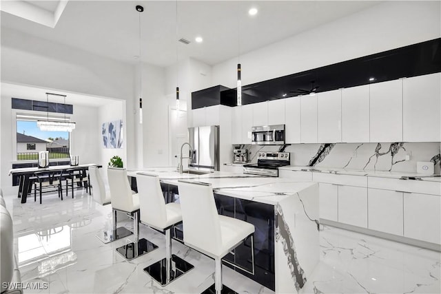 kitchen with appliances with stainless steel finishes, tasteful backsplash, white cabinetry, a breakfast bar area, and hanging light fixtures