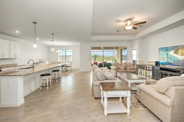 living room featuring ceiling fan with notable chandelier, a raised ceiling, and sink