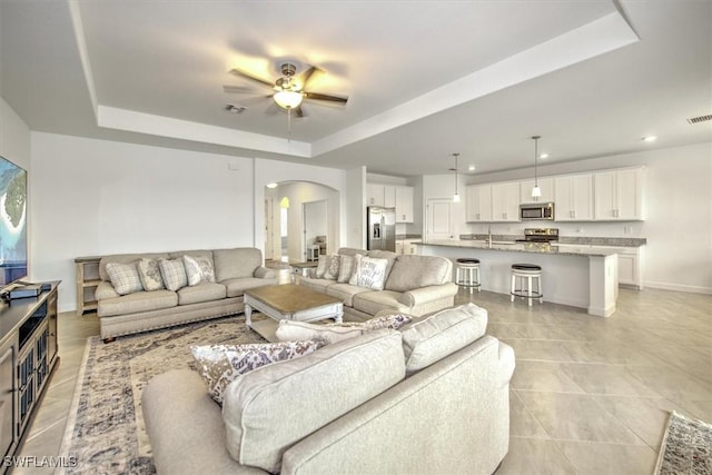 living room featuring sink, a tray ceiling, and ceiling fan