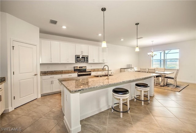 kitchen featuring stainless steel appliances, an island with sink, hanging light fixtures, and white cabinetry