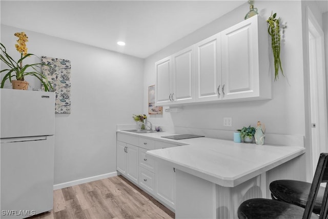 kitchen with light wood-type flooring, white refrigerator, a kitchen bar, and white cabinetry