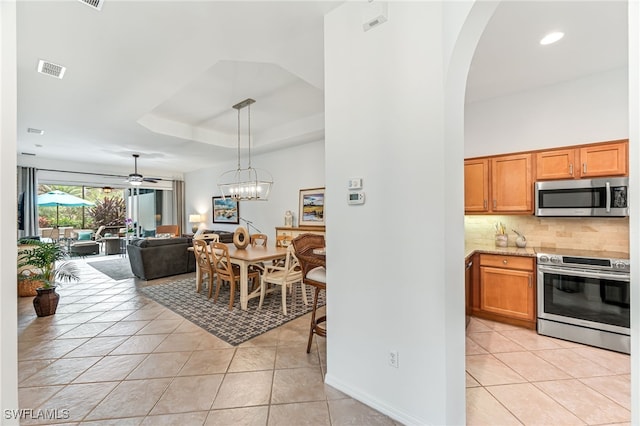 kitchen featuring decorative light fixtures, a tray ceiling, appliances with stainless steel finishes, light tile patterned floors, and ceiling fan with notable chandelier