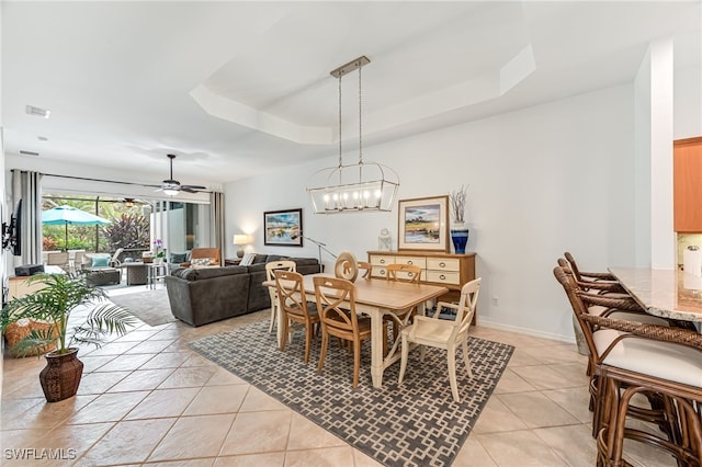 dining space with a raised ceiling, light tile patterned flooring, and ceiling fan with notable chandelier