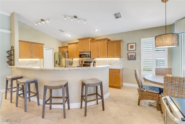 kitchen featuring light stone counters, hanging light fixtures, vaulted ceiling, and appliances with stainless steel finishes