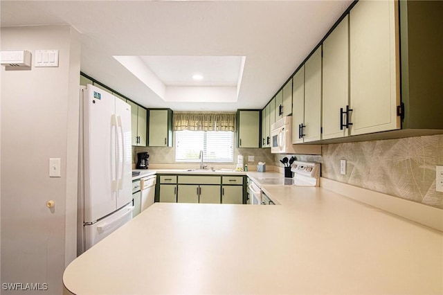 kitchen with kitchen peninsula, green cabinets, a tray ceiling, white appliances, and sink