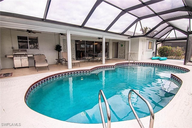 view of pool featuring glass enclosure, ceiling fan, a patio area, and an outdoor kitchen