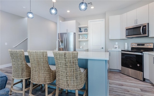 kitchen featuring decorative light fixtures, a center island, light wood-type flooring, appliances with stainless steel finishes, and white cabinets