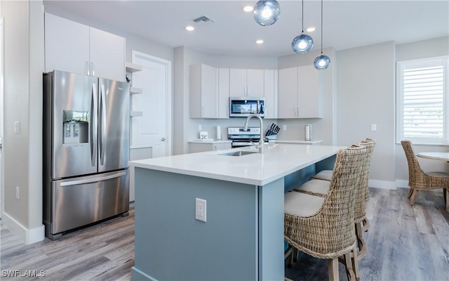 kitchen featuring white cabinetry, a center island with sink, stainless steel appliances, decorative light fixtures, and sink