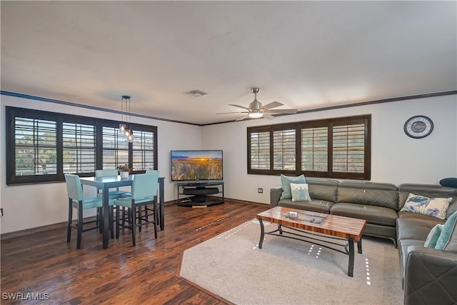 living room featuring dark hardwood / wood-style flooring, ceiling fan with notable chandelier, crown molding, and plenty of natural light