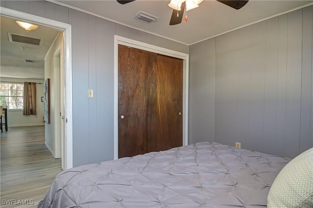 bedroom featuring a closet, wood walls, ornamental molding, light wood-type flooring, and ceiling fan