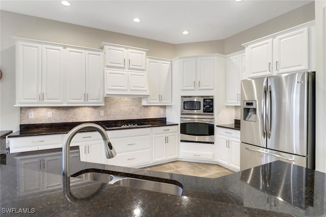 kitchen with sink, white cabinetry, appliances with stainless steel finishes, light tile patterned floors, and dark stone counters