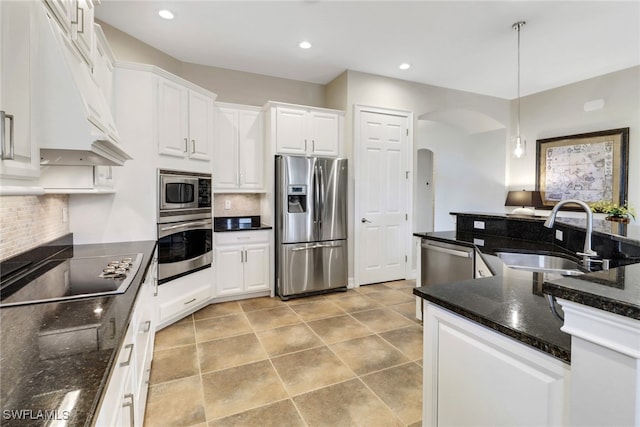 kitchen with stainless steel appliances, dark stone counters, hanging light fixtures, white cabinets, and sink