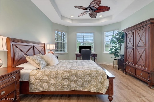 bedroom with ceiling fan, a tray ceiling, and light hardwood / wood-style flooring