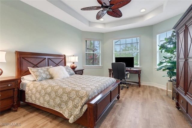 bedroom with ceiling fan, multiple windows, a tray ceiling, and light wood-type flooring