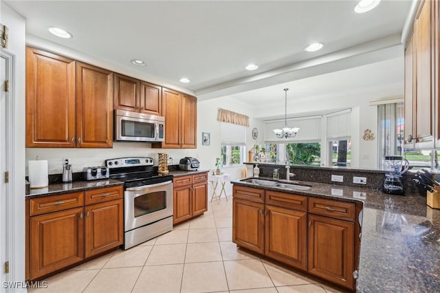 kitchen featuring sink, hanging light fixtures, light tile patterned floors, dark stone countertops, and appliances with stainless steel finishes