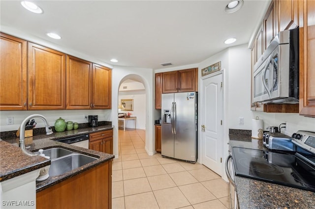 kitchen with dark stone countertops, stainless steel appliances, sink, and light tile patterned floors