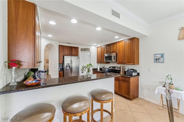 kitchen with a breakfast bar, appliances with stainless steel finishes, kitchen peninsula, and dark stone countertops