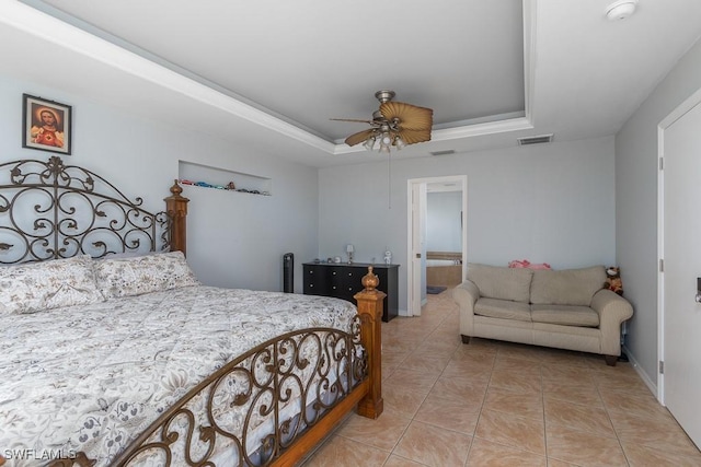 tiled bedroom featuring a raised ceiling, ensuite bath, and ceiling fan