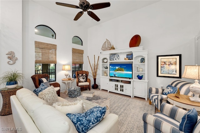 living room with light wood-type flooring, ceiling fan, and a high ceiling