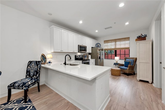 kitchen featuring white cabinets, appliances with stainless steel finishes, sink, kitchen peninsula, and light wood-type flooring