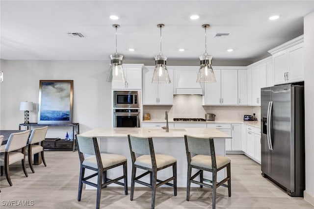 kitchen with an island with sink, stainless steel appliances, pendant lighting, white cabinets, and a breakfast bar