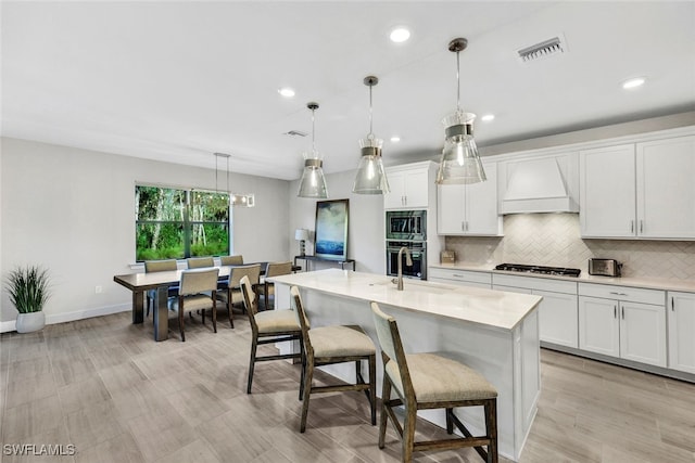 kitchen featuring pendant lighting, custom range hood, stainless steel appliances, and a kitchen island with sink