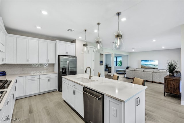 kitchen featuring decorative light fixtures, a center island with sink, sink, white cabinetry, and stainless steel appliances