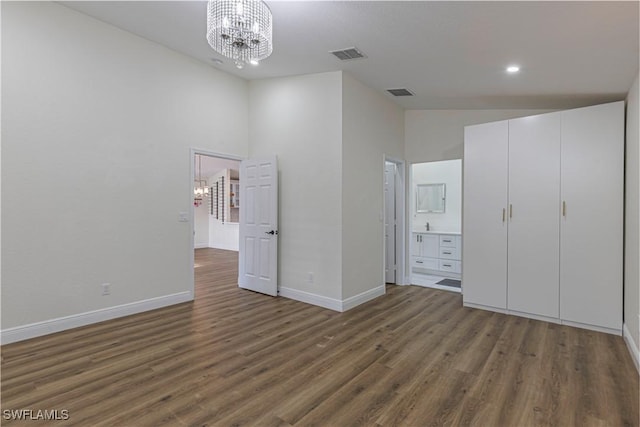 unfurnished bedroom with dark wood-type flooring, a closet, a chandelier, high vaulted ceiling, and ensuite bathroom