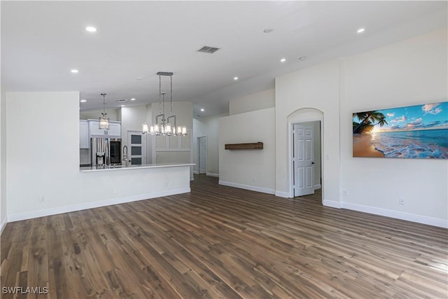 unfurnished living room with sink, dark wood-type flooring, high vaulted ceiling, and an inviting chandelier