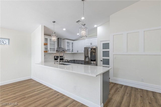 kitchen featuring appliances with stainless steel finishes, hanging light fixtures, wall chimney range hood, white cabinets, and lofted ceiling