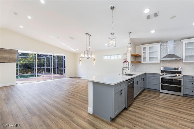 kitchen featuring vaulted ceiling, appliances with stainless steel finishes, backsplash, wall chimney exhaust hood, and gray cabinets