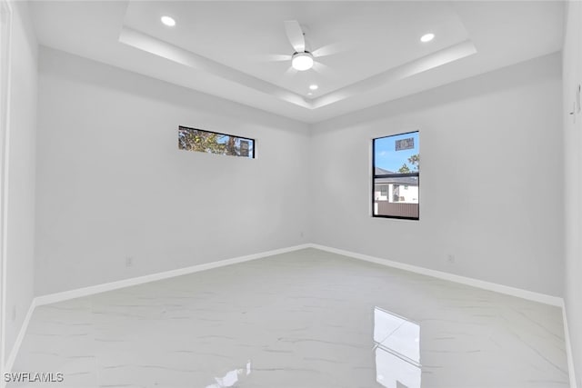 empty room with ceiling fan and a raised ceiling