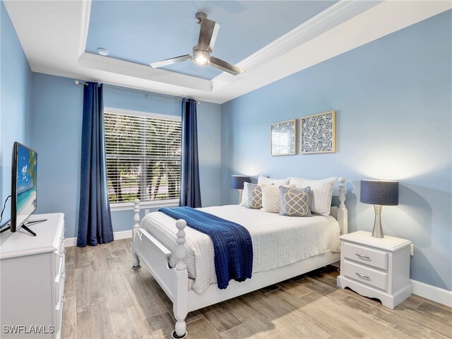 bedroom featuring ceiling fan, a tray ceiling, and light hardwood / wood-style flooring