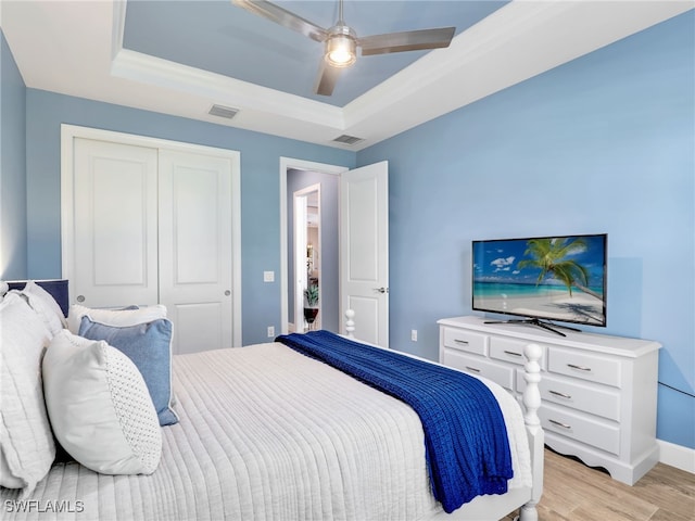 bedroom featuring ceiling fan, a raised ceiling, a closet, ornamental molding, and light hardwood / wood-style flooring