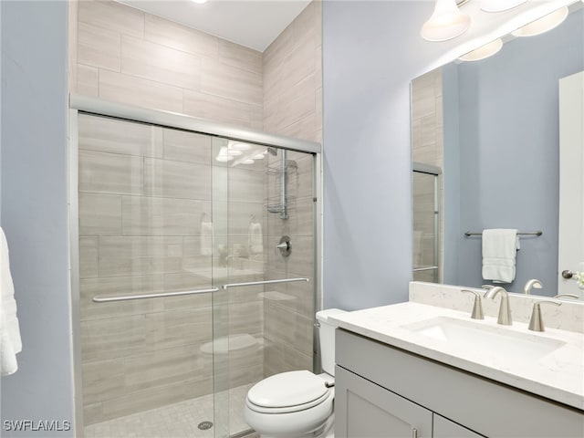 bathroom featuring a shower with shower door, toilet, and vanity