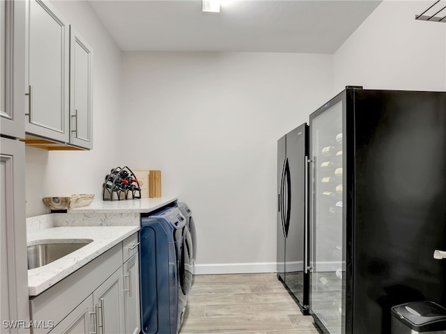 laundry area with cabinets, light wood-type flooring, sink, and washing machine and clothes dryer